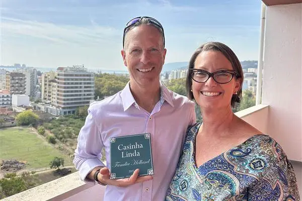 Jeff Holland and his partner on a balcony, holding a Casinha Linda Família Holland sign